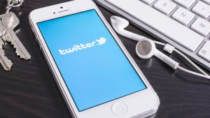 White iPhone displaying the Twitter logo next to earphones and a computer keyboard