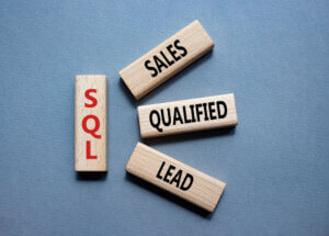 Wooden blocks spelling out SQL, Sales, Qualified, and Lead on a blue background